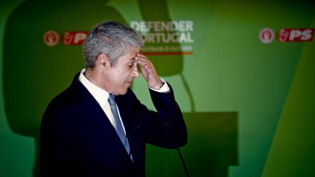 Ein Mann im Anzug steht vor einem grünen Hintergrund mit der Aufschrift „Defender Portugal“.