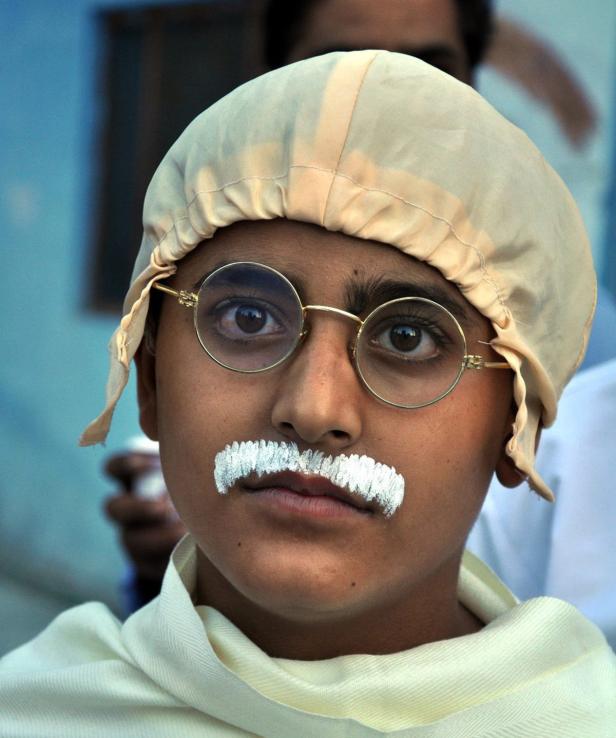 Ein Kind, verkleidet als Mahatma Gandhi, mit Brille und aufgemaltem Schnurrbart.
