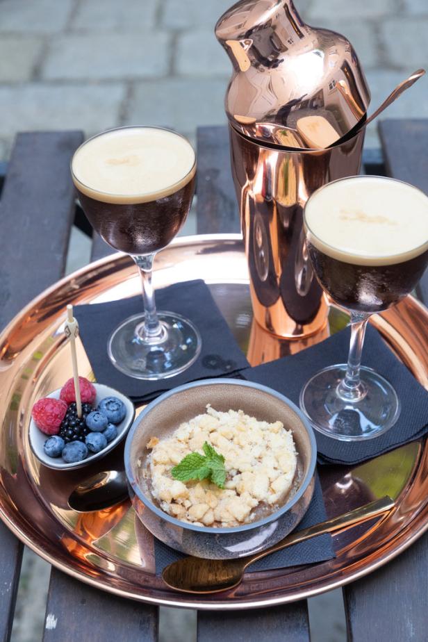 Auf einem Tablett stehen zwei Espresso Martinis, ein Crumble und eine Schale mit Beeren.