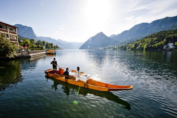 Ein Paar speist in einem Boot auf einem See, während ein Mann das Boot rudert.