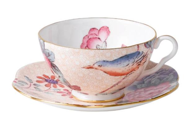 Eine Teetasse mit Vogel- und Blumenmuster steht auf einer Untertasse.