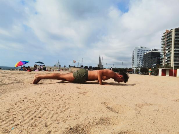Ein Mann macht Liegestütze am Strand von Barcelona.