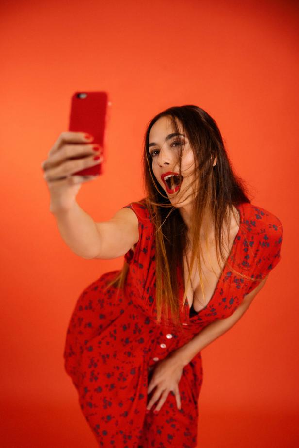 Eine Frau im roten Kleid macht ein Selfie vor einem roten Hintergrund.
