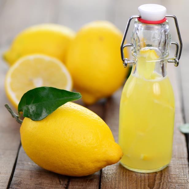 Eine Flasche Limonade und mehrere Zitronen auf einem Holztisch.