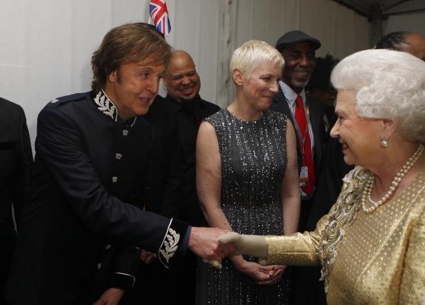 Königin Elisabeth II. schüttelt Paul McCartney die Hand, Annie Lennox steht daneben.