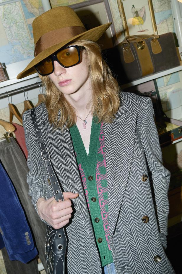 Ein Mann mit Hut und Sonnenbrille trägt einen Blazer und eine Handtasche.