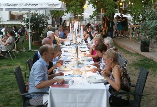 Gäste sitzen an einer langen Tafel im Freien und speisen.