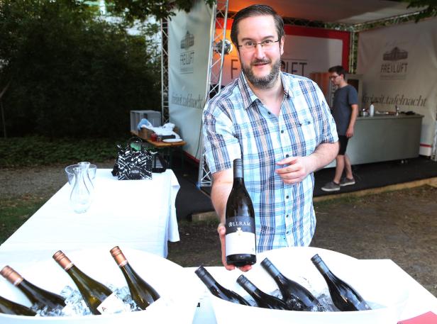 Ein Mann präsentiert eine Flasche Allram-Wein vor einer Eiswanne mit weiteren Flaschen.