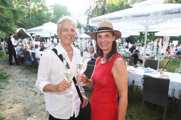 Ein Mann und eine Frau stoßen auf einer Gartenparty mit Sektgläsern an.