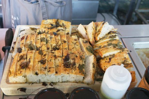 Geschnittenes Focaccia-Brot mit Kräutern auf einem Holzbrett.