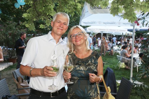 Ein Mann und eine Frau posieren mit Getränken auf einer Gartenparty.