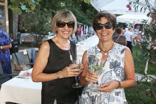 Zwei Frauen mit Sonnenbrillen halten Getränke bei einer Gartenparty.