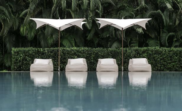 Vier Liegestühle mit Sonnenschirmen stehen an einem ruhigen, türkisfarbenen Pool.