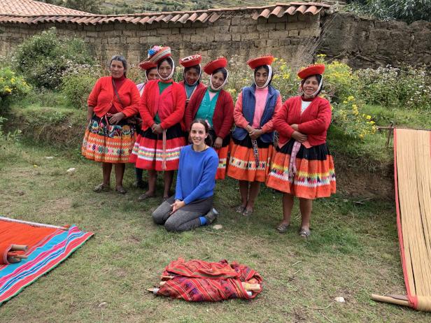 Eine Frau kniet vor einer Gruppe peruanischer Weberinnen in traditioneller Kleidung.