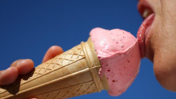 Eine Person schleckt ein rosa Erdbeereis in einer Waffel vor blauem Himmel.