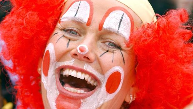 Eine Frau mit roter Perücke und Clownsgesicht lacht in die Kamera.