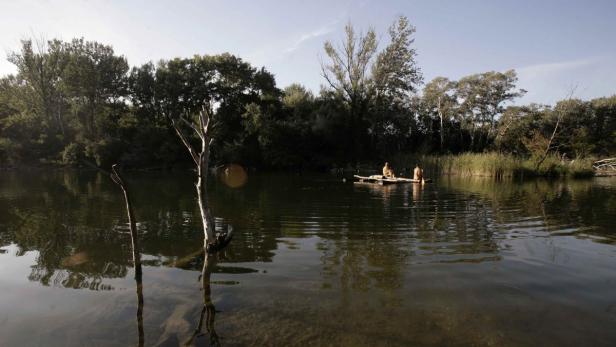 Zwei Personen sitzen auf einem Floß auf einem ruhigen Fluss.