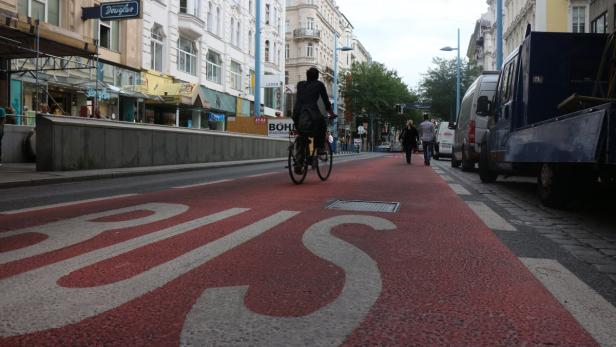 Eine Person fährt mit dem Fahrrad auf einem rot markierten Radweg in einer Stadt.