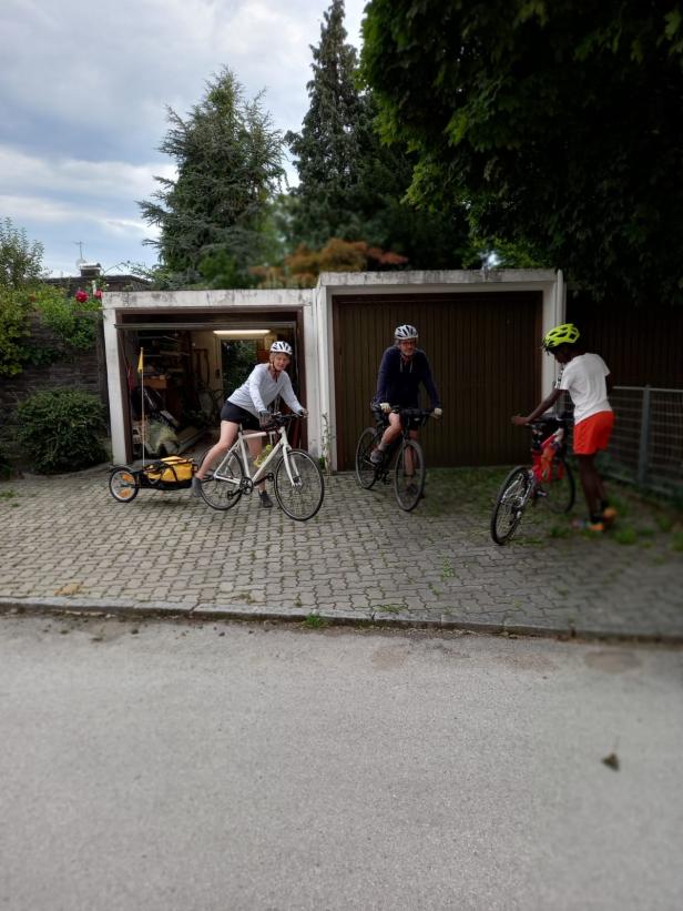 Drei Personen mit Fahrrädern stehen vor Garagen.
