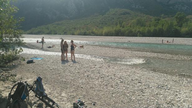 Menschen entspannen an einem sonnigen Tag an einem Flussufer mit Kiesstrand.