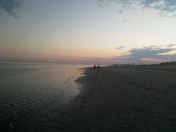 Zwei Personen spazieren bei Sonnenuntergang am Strand entlang.