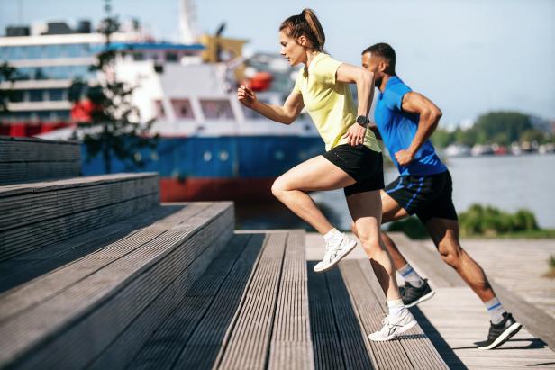 Eine Frau und ein Mann joggen eine Holztreppe hinauf.