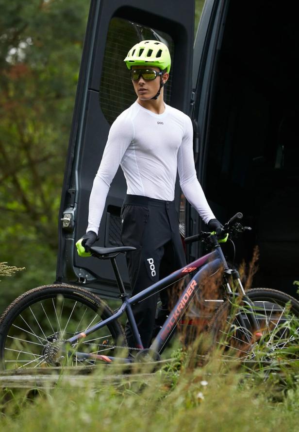 Ein Mountainbiker mit Helm und Brille steht neben seinem Fahrrad vor einem Transporter.