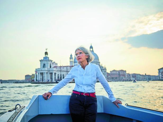 Eine ältere Frau fährt mit einem Boot durch Venedig und blickt in die Ferne.