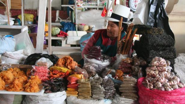 Eine Frau mit Hut verkauft Lebensmittel und Gewürze auf einem Marktstand.