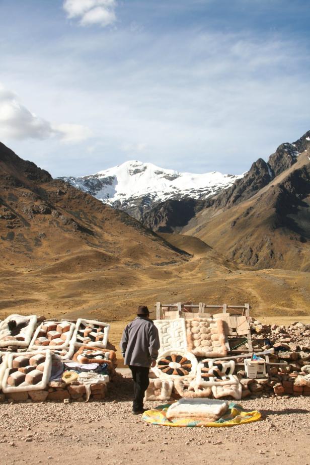 Ein Mann betrachtet einen Stand mit Teppichen vor einer Bergkulisse.