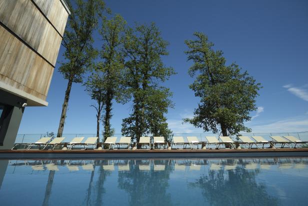 Ein Schwimmbad mit Liegestühlen und Bäumen unter blauem Himmel.