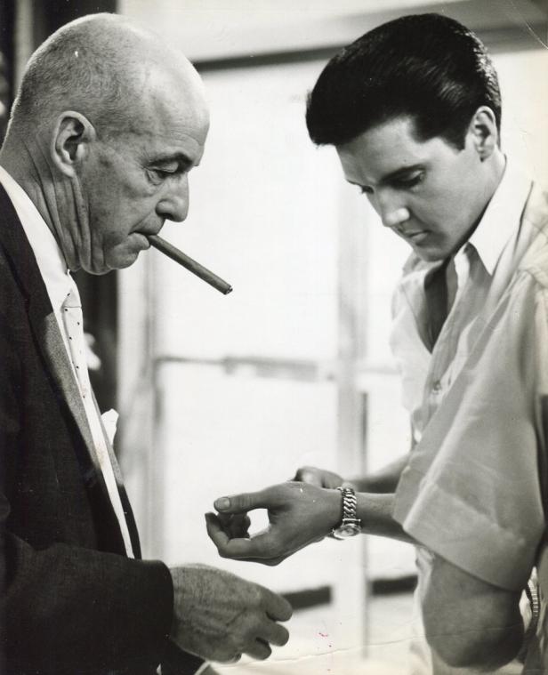 Elvis Presley betrachtet das Handgelenk eines Mannes mit Zigarre.