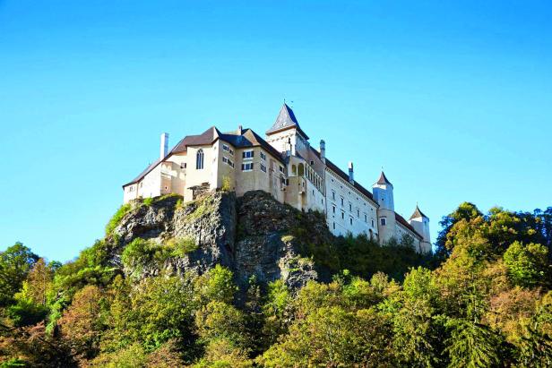 Burg Kreuzenstein thront auf einem Felsen über bewaldeten Hügeln.