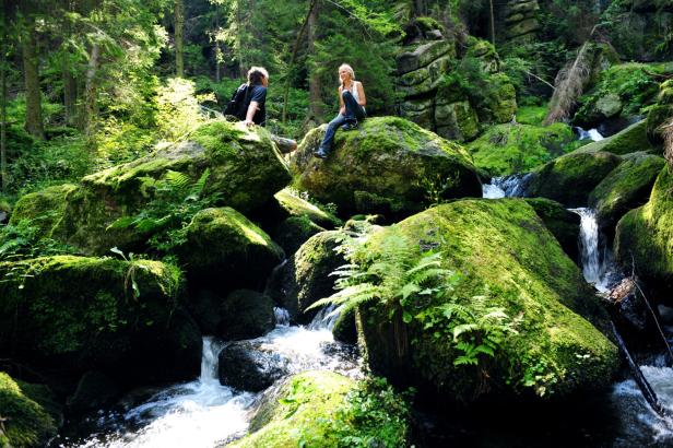 Ein Mann und eine Frau sitzen auf moosbedeckten Felsen an einem Bach.