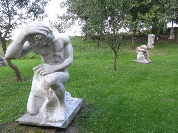 Eine Skulptur eines Mannes, der seinen Kopf in den Händen hält, steht in einem Park.