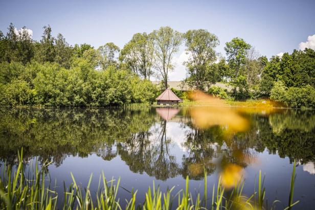 Ein kleines Haus mit rotem Dach spiegelt sich in einem ruhigen See.