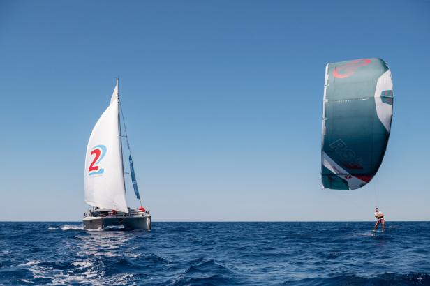Ein Segelboot und ein Kitesurfer auf dem offenen Meer.
