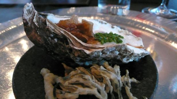 Eine Auster mit einer Füllung und frittierten Gemüsestreifen auf einem Teller.