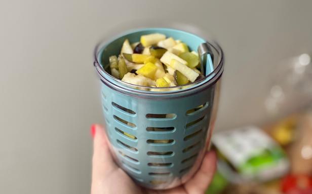 Eine Hand hält einen Behälter mit geschnittenem Obst, darunter Äpfel und Birnen.