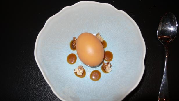 Ein pochiertes Ei mit Sauce und Trüffeln in einer hellblauen Schale.