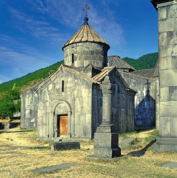 Das Kloster Haghartsin in Armenien mit seiner steinernen Architektur und dem grünen Hügel im Hintergrund.