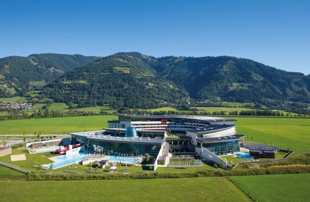Ein großes Hotelresort mit Pools liegt vor einer grünen Hügellandschaft.