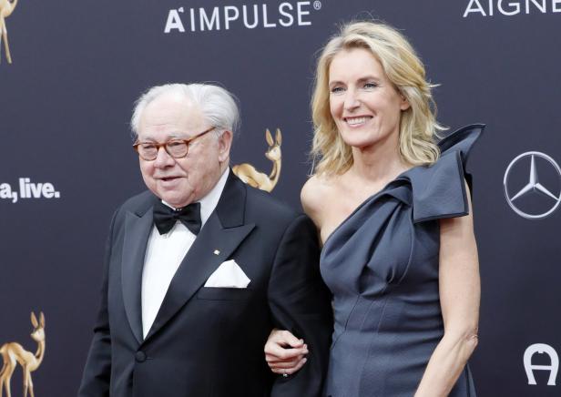 Ein älterer Mann im Smoking und eine blonde Frau im Abendkleid auf dem roten Teppich.