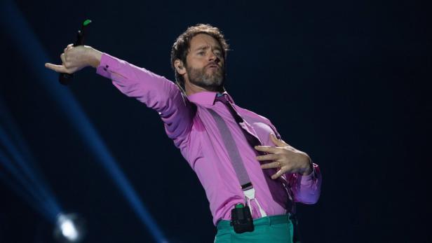 Ein Mann mit Bart singt mit einem Mikrofon in der Hand auf einer Bühne.