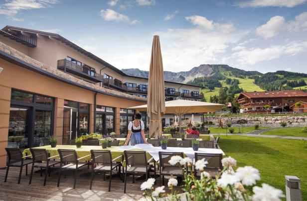 Eine Frau in Tracht deckt im Außenbereich eines Hotels die Tische ein.