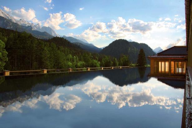 Ein Infinity-Pool spiegelt die umliegenden Berge und den bewaldeten Himmel wider.