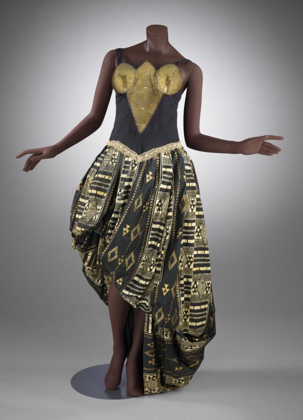 Ein ärmelloses Kleid mit goldenem Brustpanzer und einem Rock mit geometrischen Mustern auf einer Schaufensterpuppe.