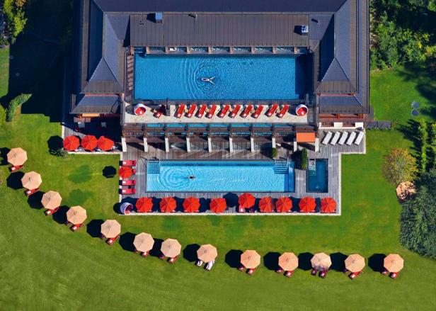 Luftaufnahme eines Luxusresorts mit zwei Pools, Liegestühlen und Sonnenschirmen auf einer grünen Wiese.