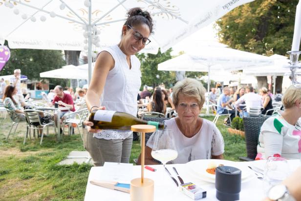 Eine Kellnerin schenkt einer älteren Dame im Freien Wein ein.