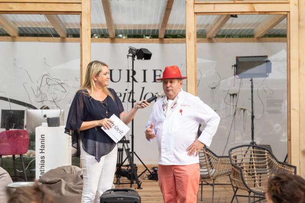 Eine Frau interviewt einen Mann mit rotem Hut auf einer Bühne.